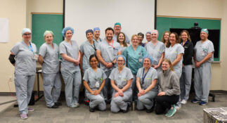 Group of nurses wearing light blue scrubs, all smiling in a classroom. 